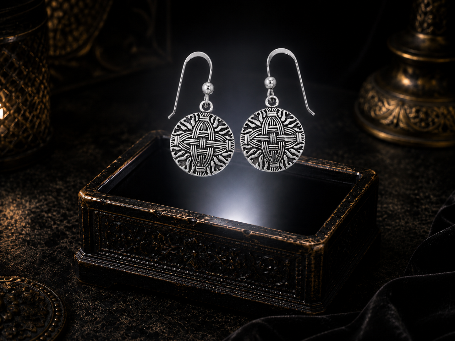 Sterling silver St. Brigid’s Celtic cross earrings floating above a glowing ornate jewelry box in a dark luxury setting