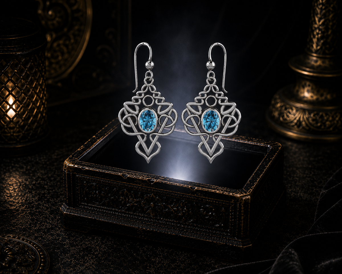 Sterling silver Celtic filigree knot drop earrings with blue topaz gemstones floating above a glowing ornate jewelry box in a dark luxury setting