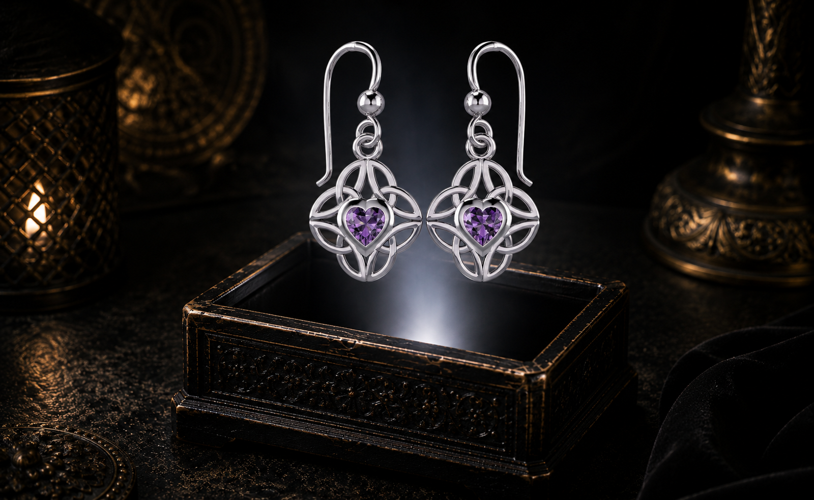 Sterling silver Celtic heart earrings with four interconnected Triquetra knots and garnet gemstones floating above an ornate jewelry box in a dark luxury jewelry display with mystical illumination.