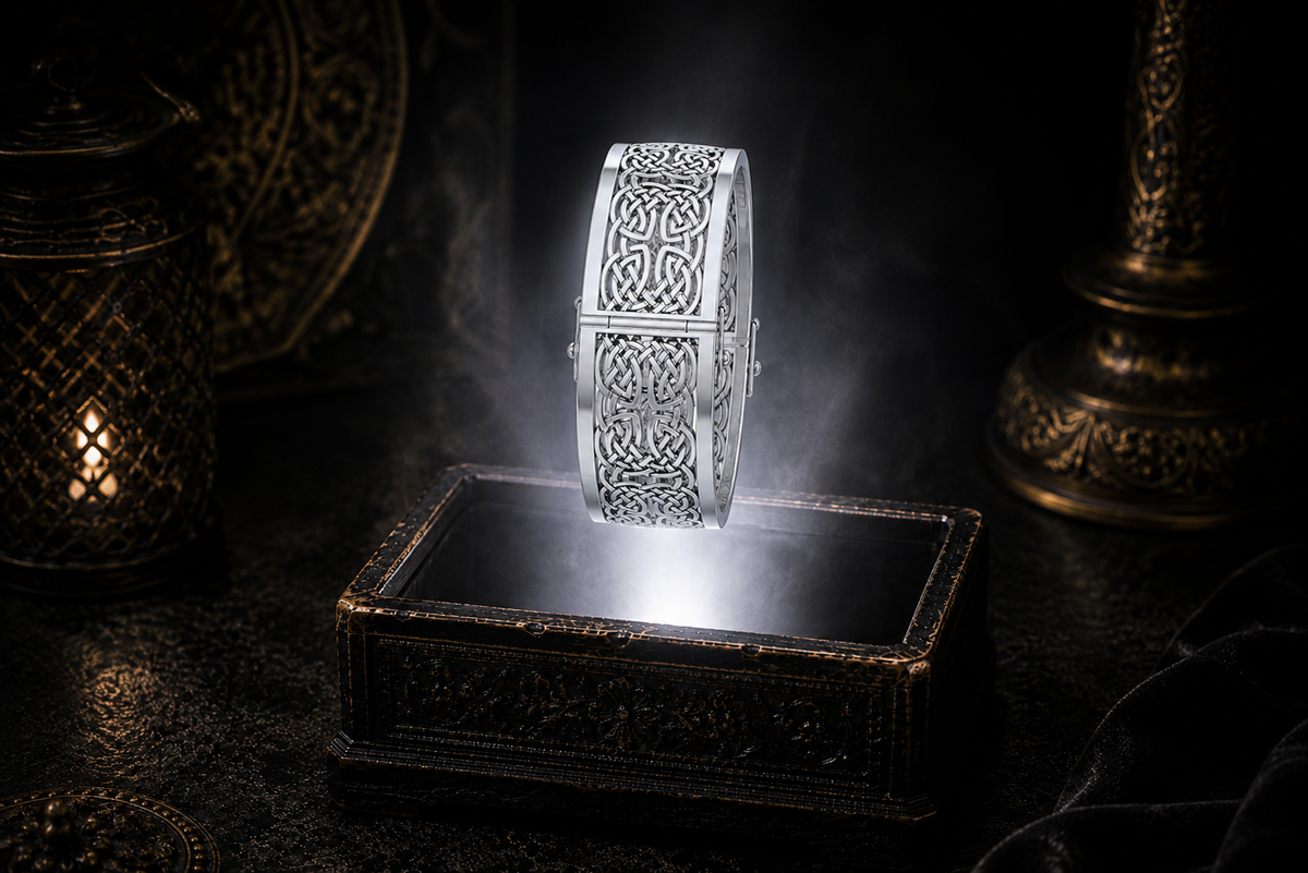 Wide sterling silver hollow Celtic knotwork bangle bracelet with intricate see-through design floating above an ornate black jewelry box illuminated by soft white light in a dark luxury setting with a refined cinematic atmosphere.