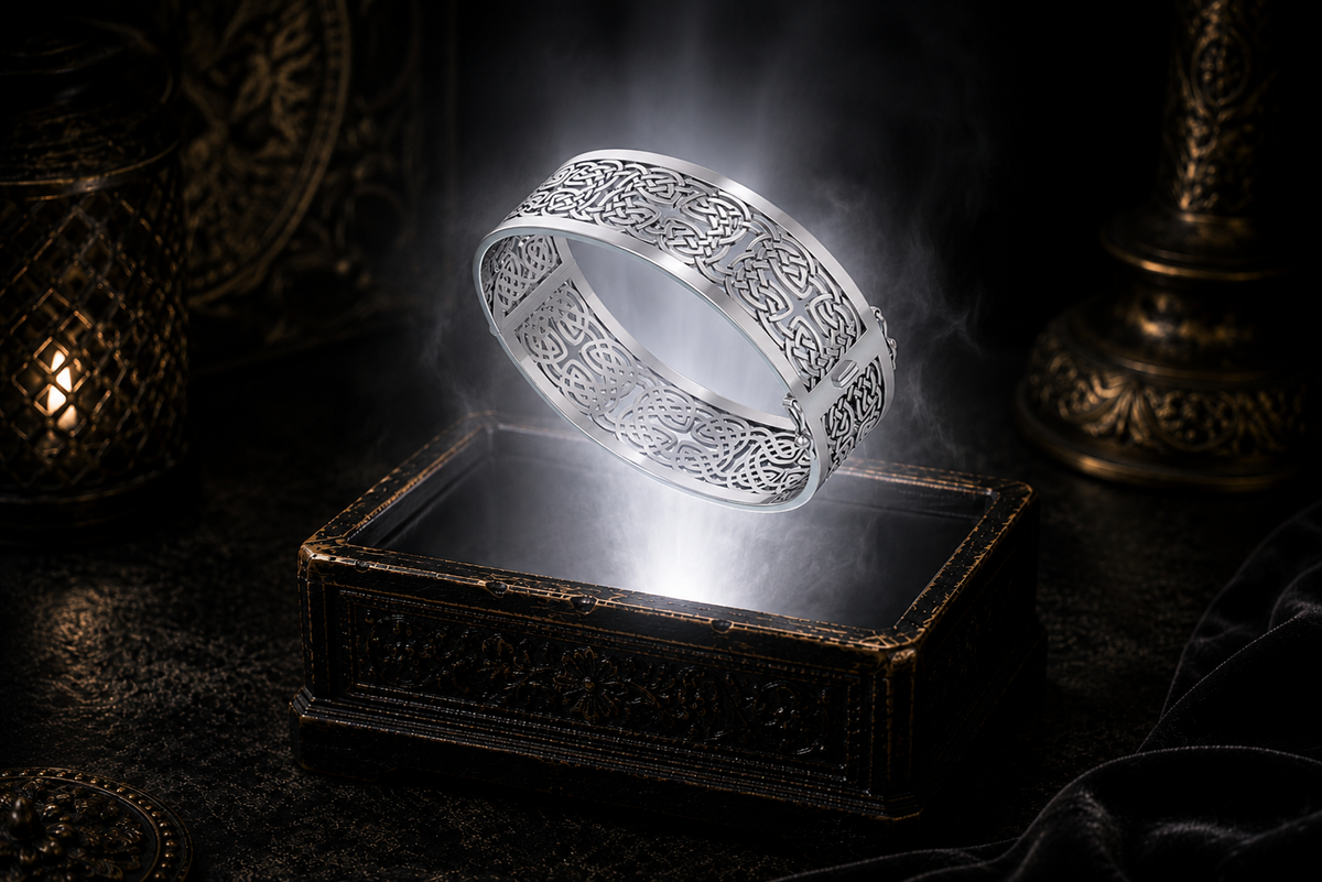 Wide sterling silver hollow Celtic knotwork bangle bracelet with intricate see-through design floating above an ornate black jewelry box illuminated by soft white light in a dark luxury setting with a refined cinematic atmosphere.