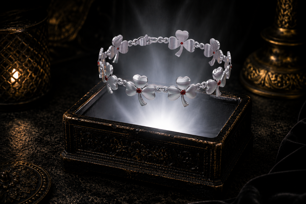 Sterling silver shamrock link bracelet with garnet accent gemstones floating above an ornate black jewelry box illuminated by soft white light in a dark luxury Irish-inspired setting.