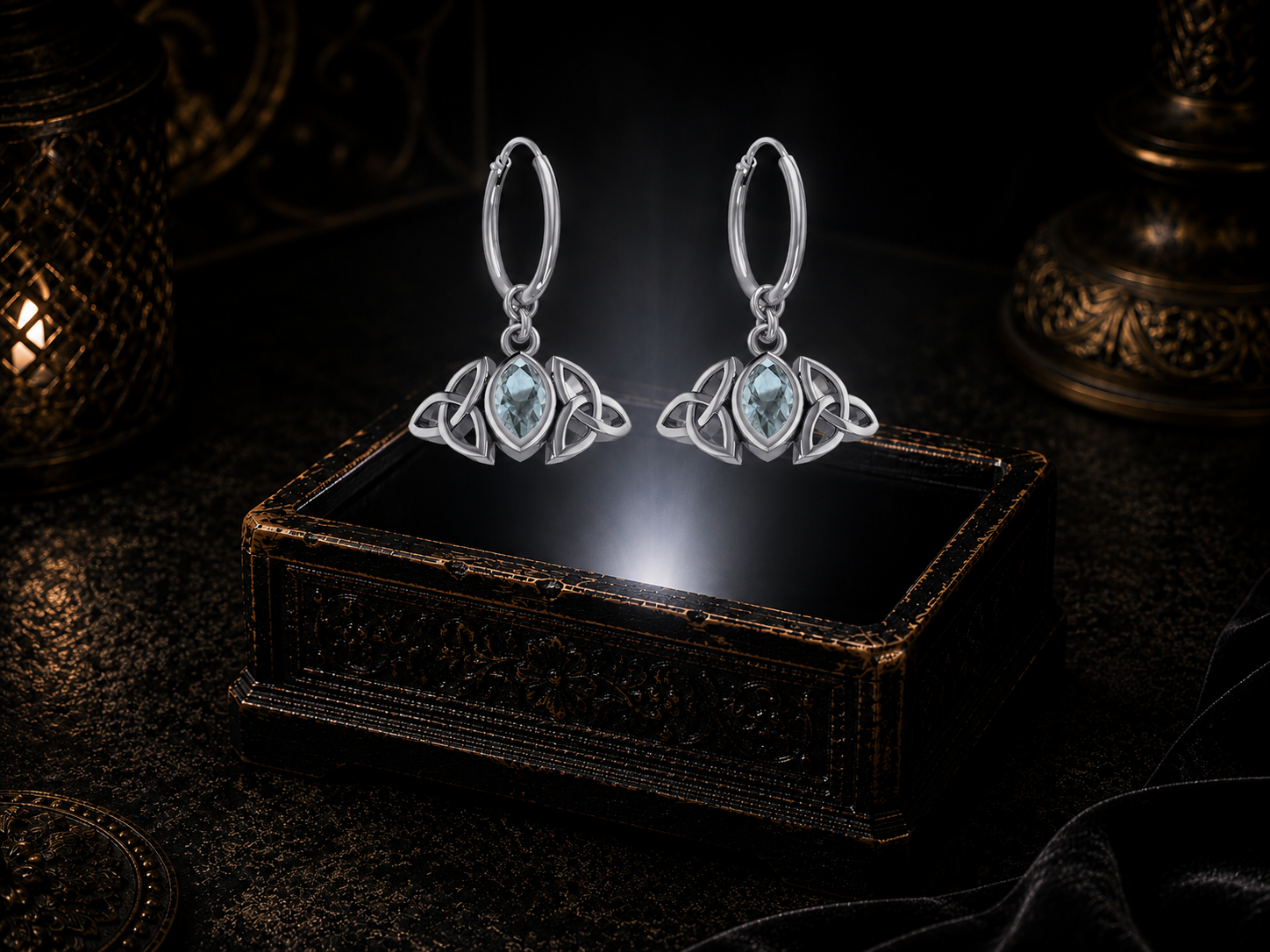 Sterling silver Triquetra hoop earrings with garnet gemstones floating above a glowing ornate jewelry box in a dark luxury setting