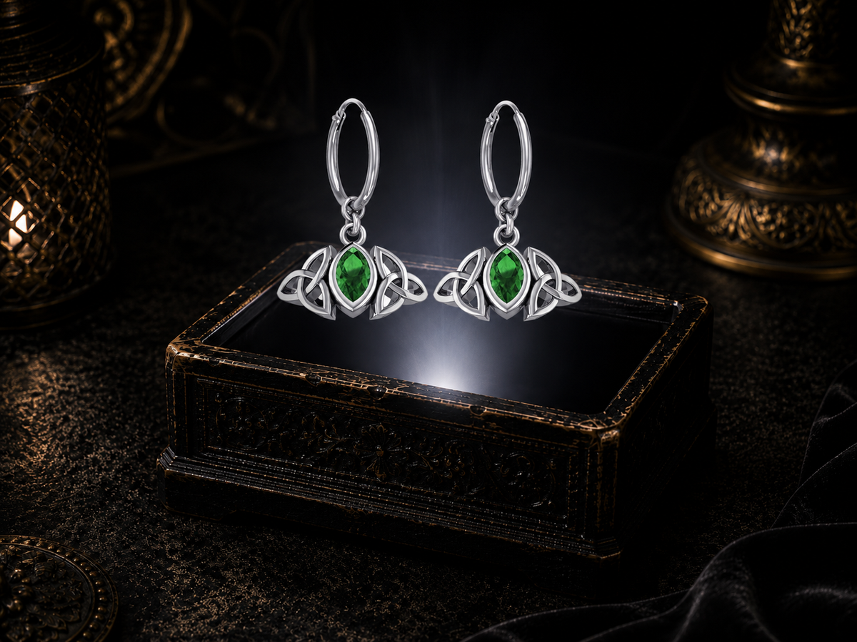 Sterling silver Triquetra charm hoop earrings with emerald glass gemstones floating above a glowing ornate jewelry box in a dark luxury setting