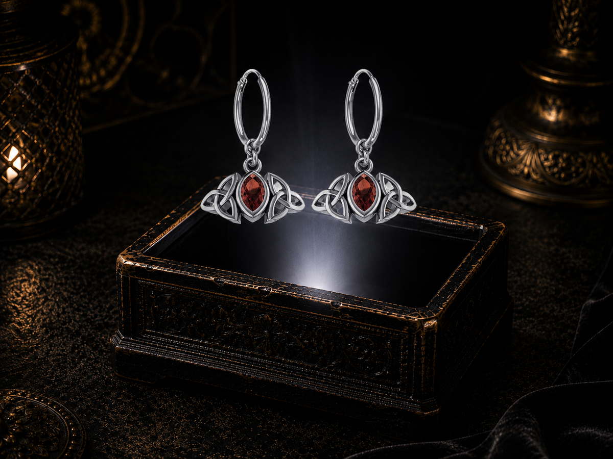 Sterling silver Triquetra charm hoop earrings with garnet gemstones floating above a glowing ornate jewelry box in a dark luxury setting