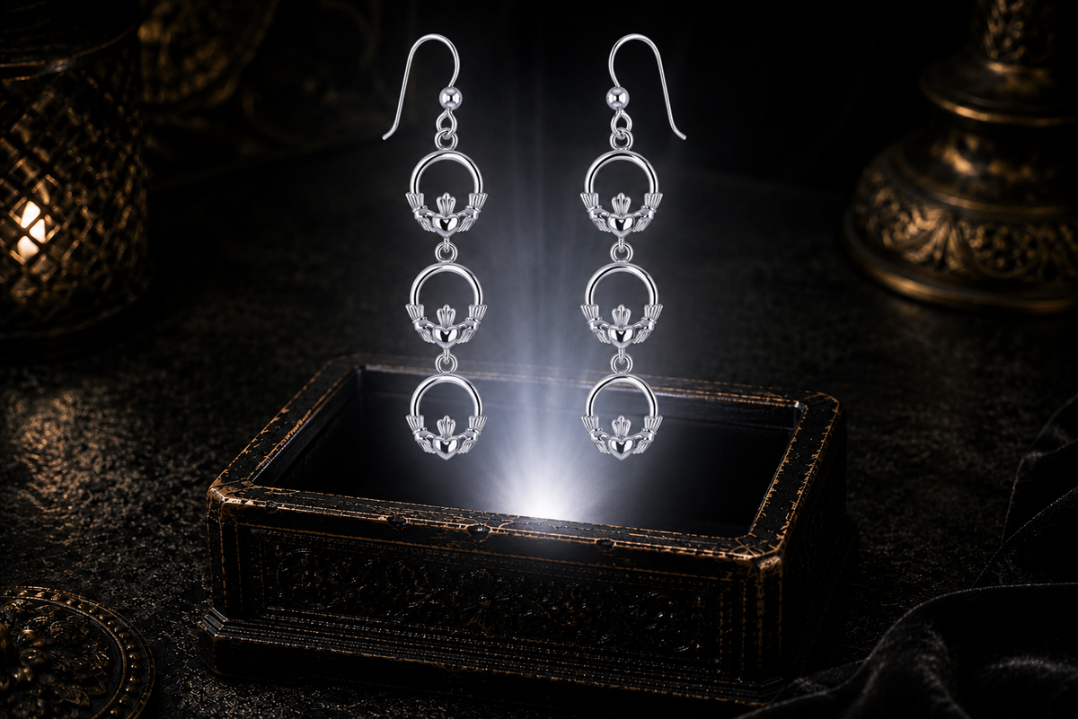 Triple sterling silver Claddagh dangle earrings floating above a dark ornate jewelry box with glowing white light in a mystical gothic luxury setting