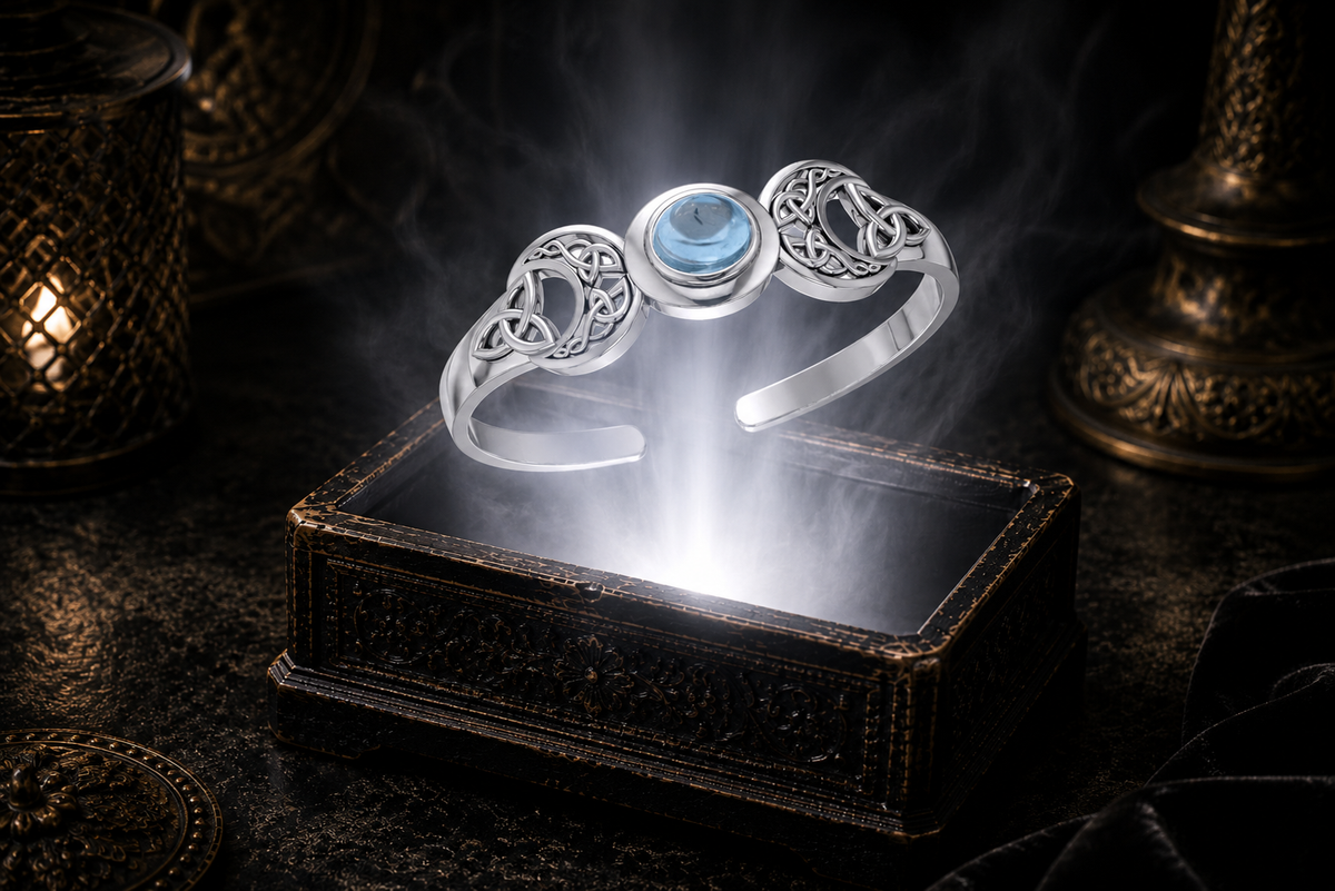 Sterling silver Triple Moon Celtic knot cuff bracelet with blue topaz gemstone floating above an ornate jewelry box illuminated by soft white light in a dark luxury setting with mystical lunar symbolism and cinematic elegance.