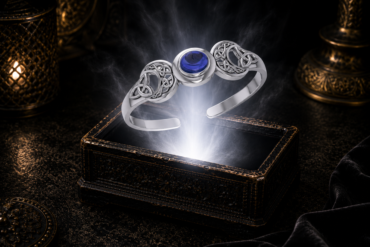 Sterling silver Triple Moon Celtic knot cuff bracelet with sapphire gemstone floating above an ornate jewelry box illuminated by soft white light in a dark luxury setting with mystical lunar symbolism and cinematic elegance.
