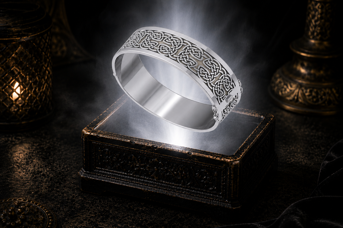 Wide sterling silver Celtic knotwork hinged bangle bracelet floating above an ornate black jewelry box illuminated by soft white light in a dark luxury setting with refined Celtic elegance and cinematic atmosphere.