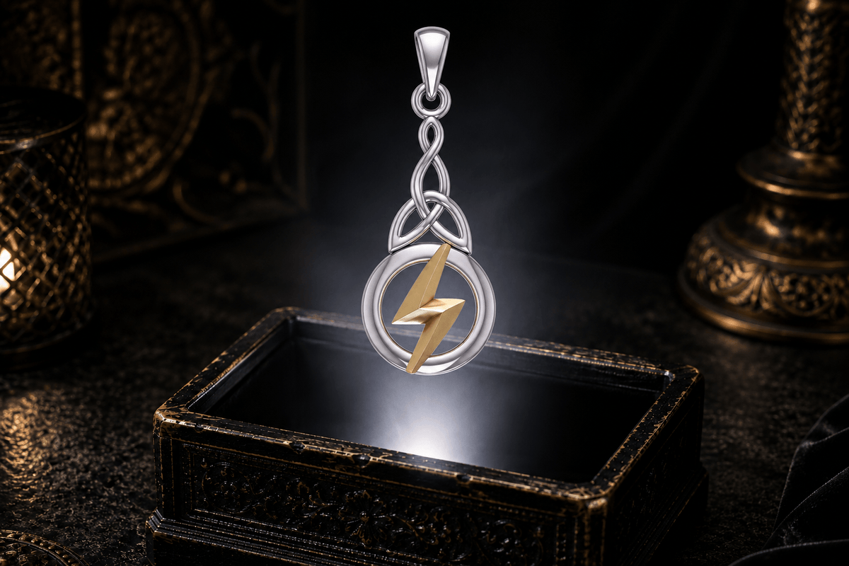 Sterling silver Celtic knot pendant with a gold Zeus lightning bolt hovering above an ornate black jewelry box in a neutral white beam.