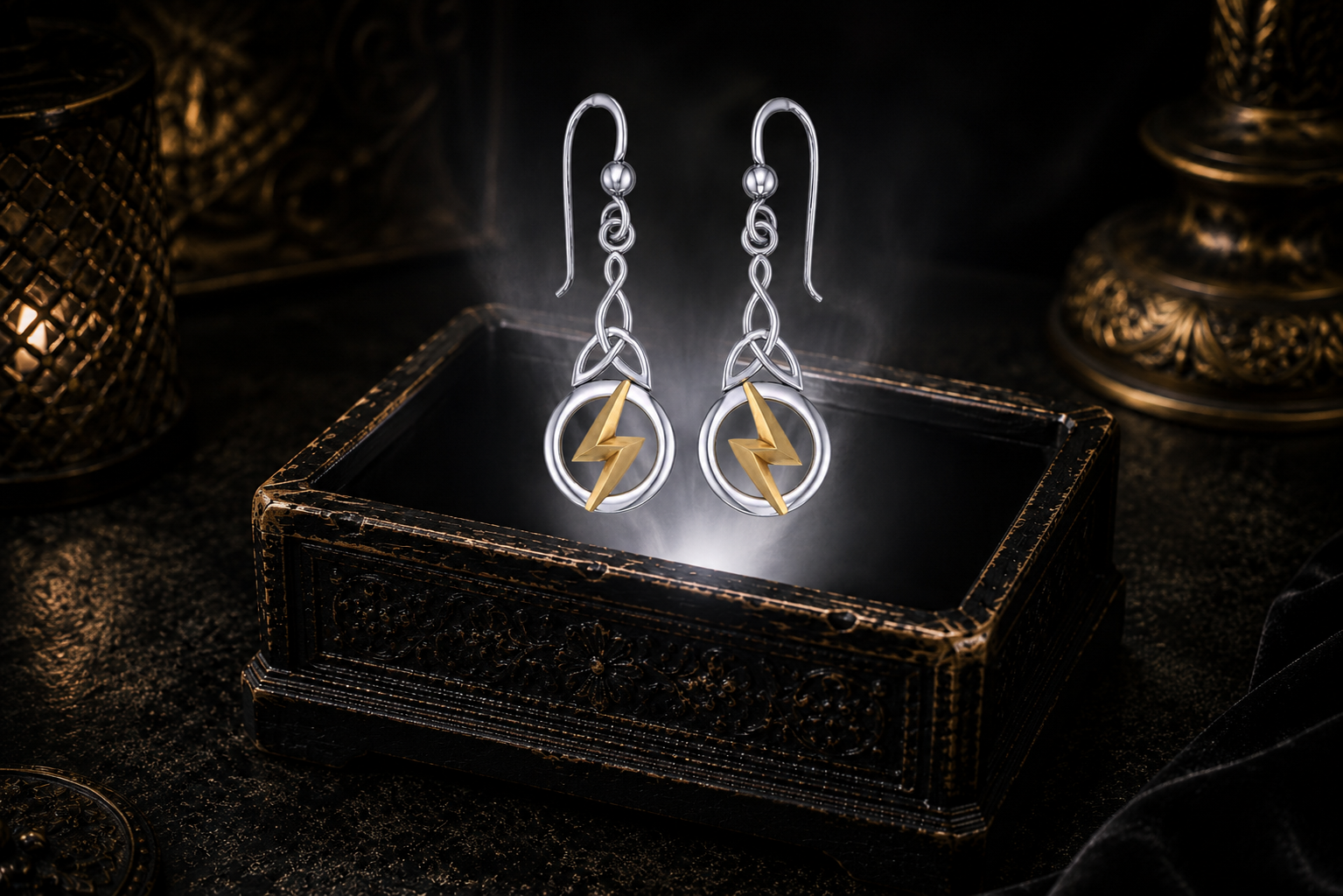Sterling silver Triquetra lightning bolt earrings with 14K gold accents floating above a glowing ornate jewelry box in a dark luxury setting